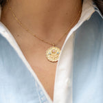 scalloped edge round pendant gold charm with a floral bloom and blue and pink gemstones on a gold chain on a woman's neck