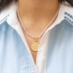 pink stone beaded necklace with a gold floral pendant with pink gemstones on a woman's neck