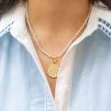 pink stone beaded necklace with a gold floral pendant with pink gemstones on a woman's neck