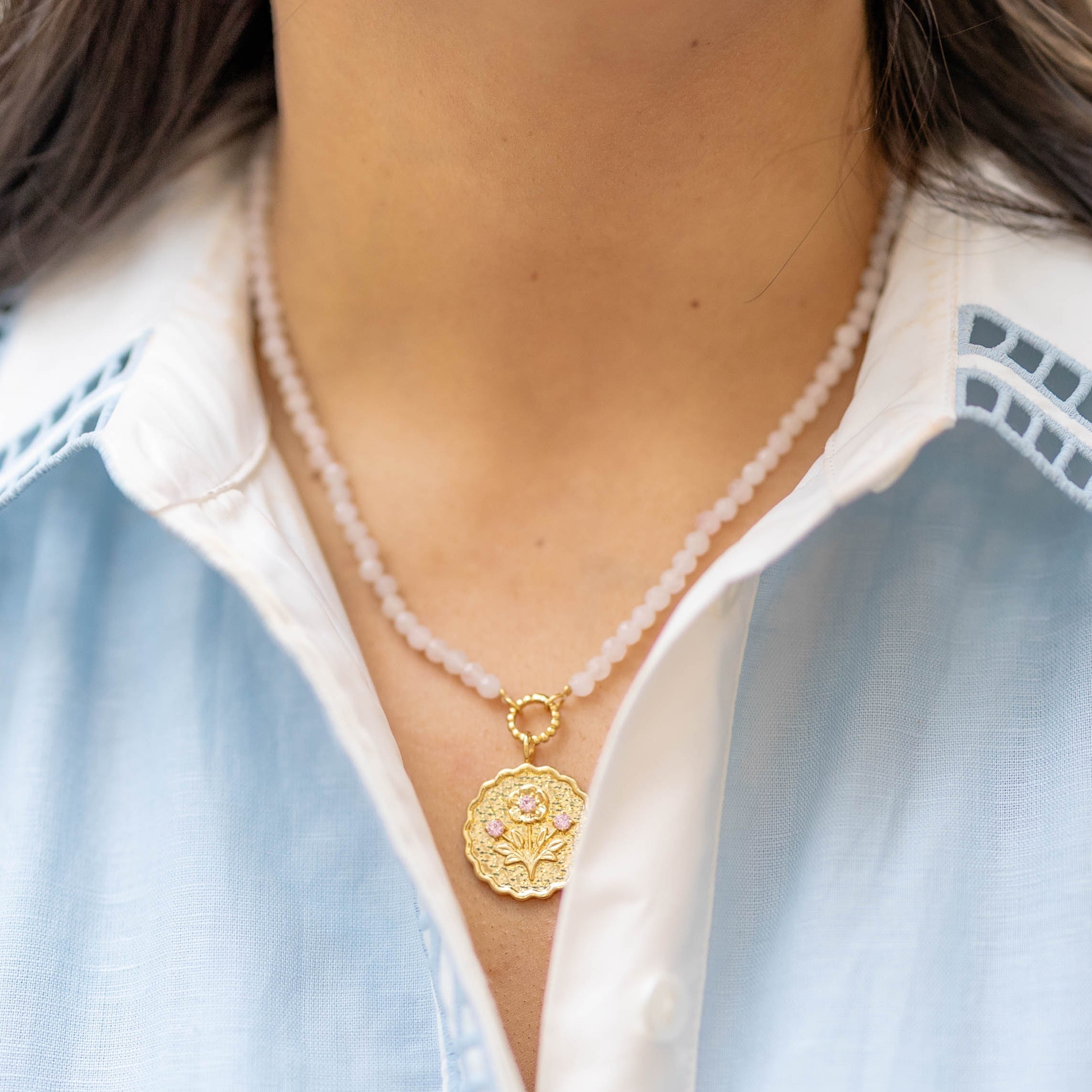 pink stone beaded necklace with a gold floral pendant with pink gemstones on a woman's neck
