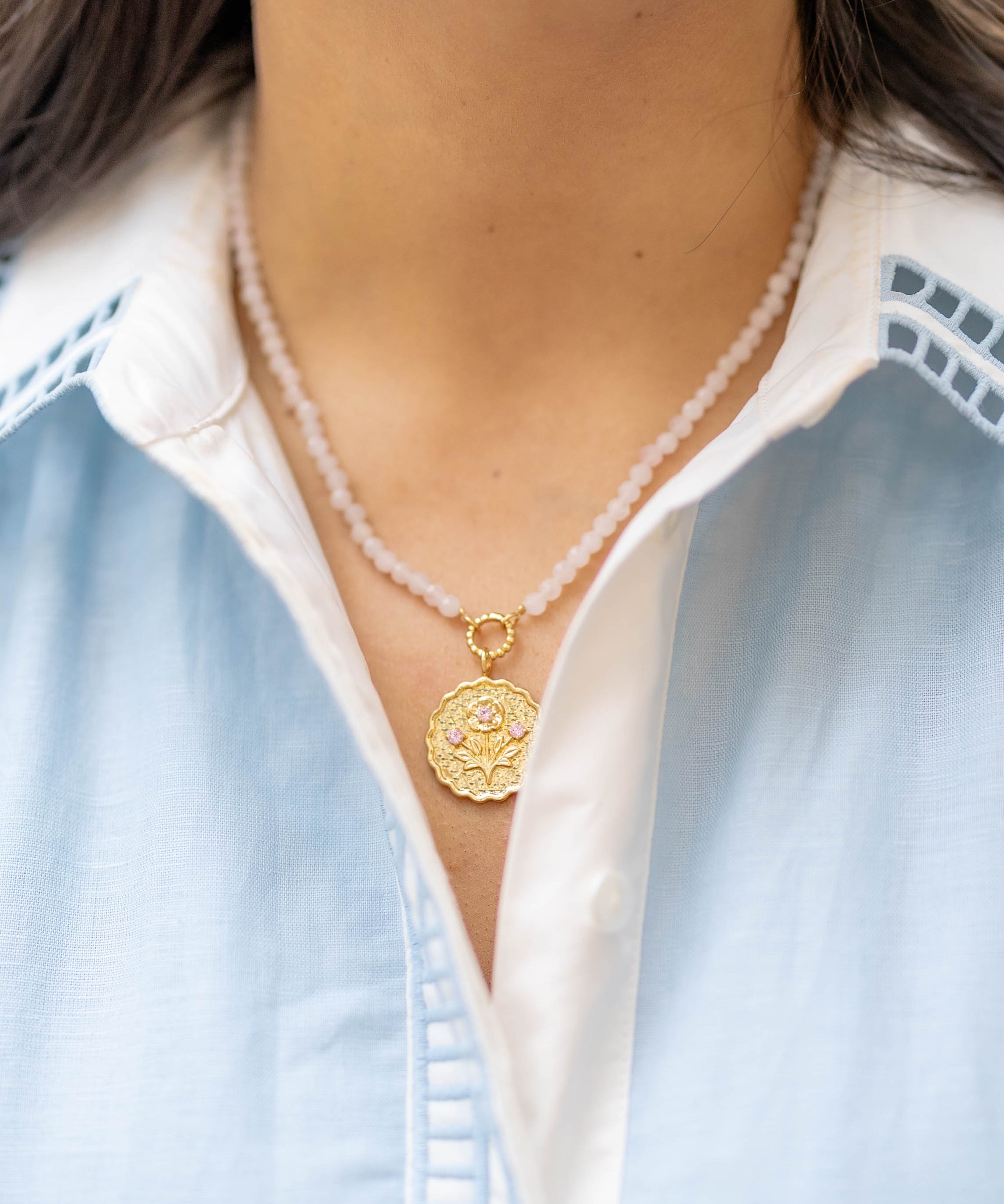 pink stone beaded necklace with a gold floral pendant with pink gemstones on a woman's neck