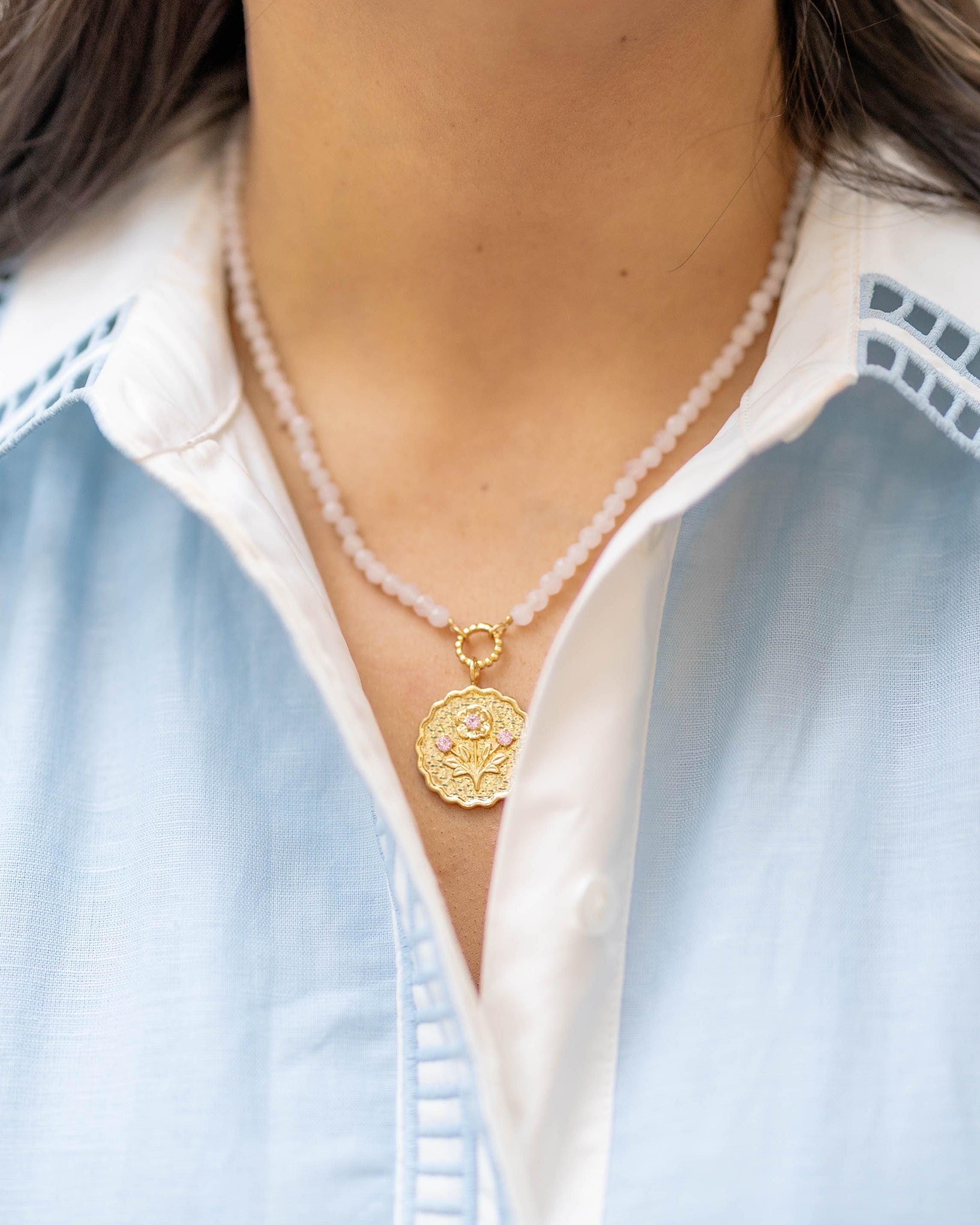 pink stone beaded necklace with a gold floral pendant with pink gemstones on a woman's neck