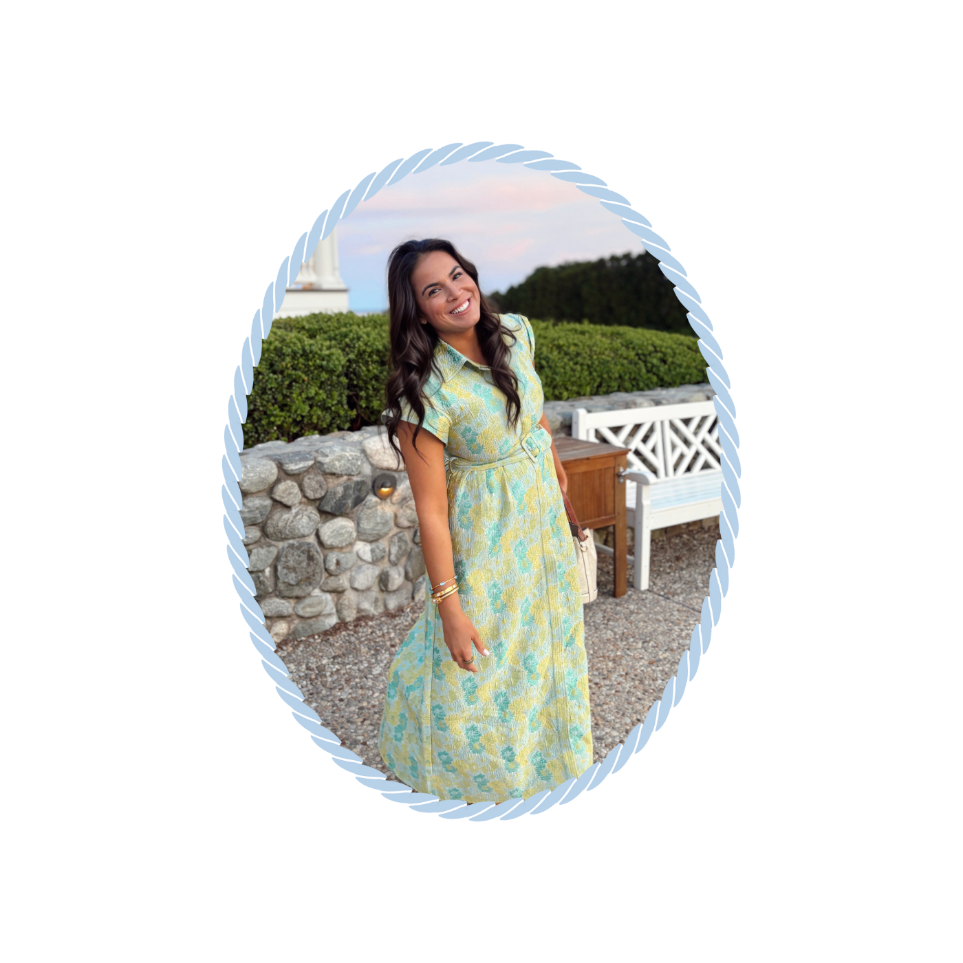 Alexa in a floral dress standing outdoors with greenery and a stone wall in the background