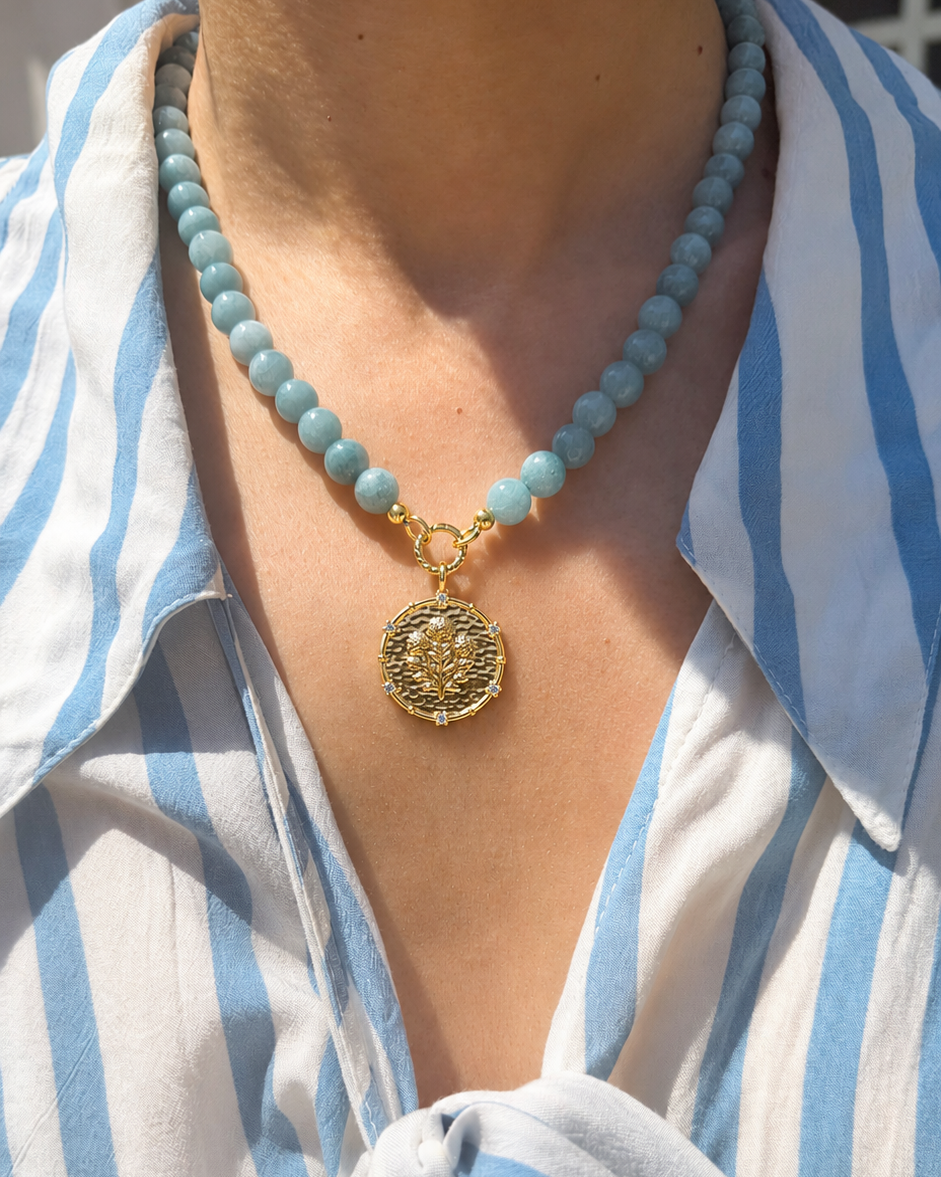 Necklace with a gold pendant worn by a person in a blue and white striped shirt.