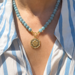 Necklace with a gold pendant worn by a person in a blue and white striped shirt.