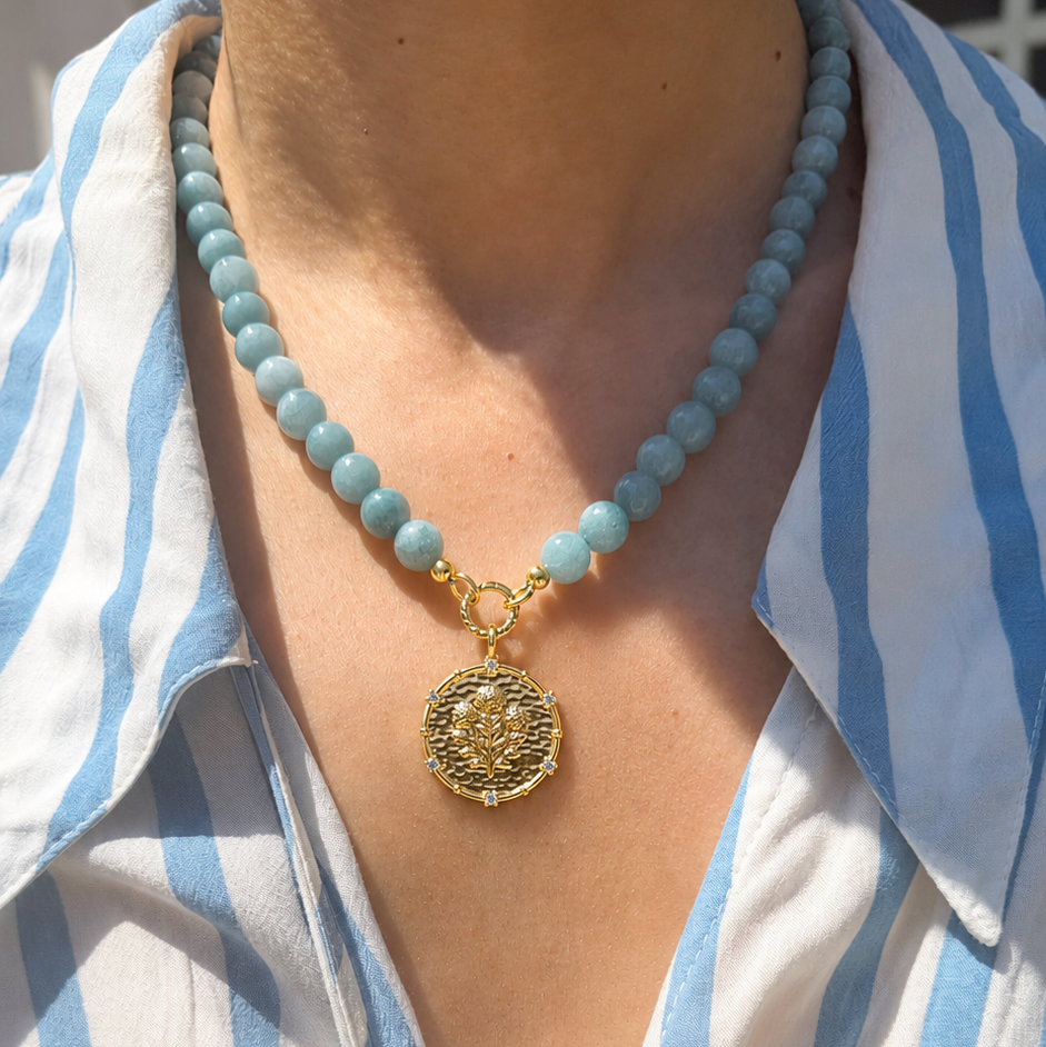 Necklace with a gold pendant worn by a person in a blue and white striped shirt.