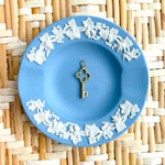 Decorative blue plate with white floral patterns and a golden key charm on a woven mat background