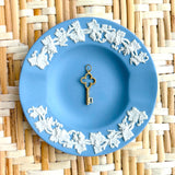 Decorative blue plate with white floral patterns and a golden key charm on a woven mat background