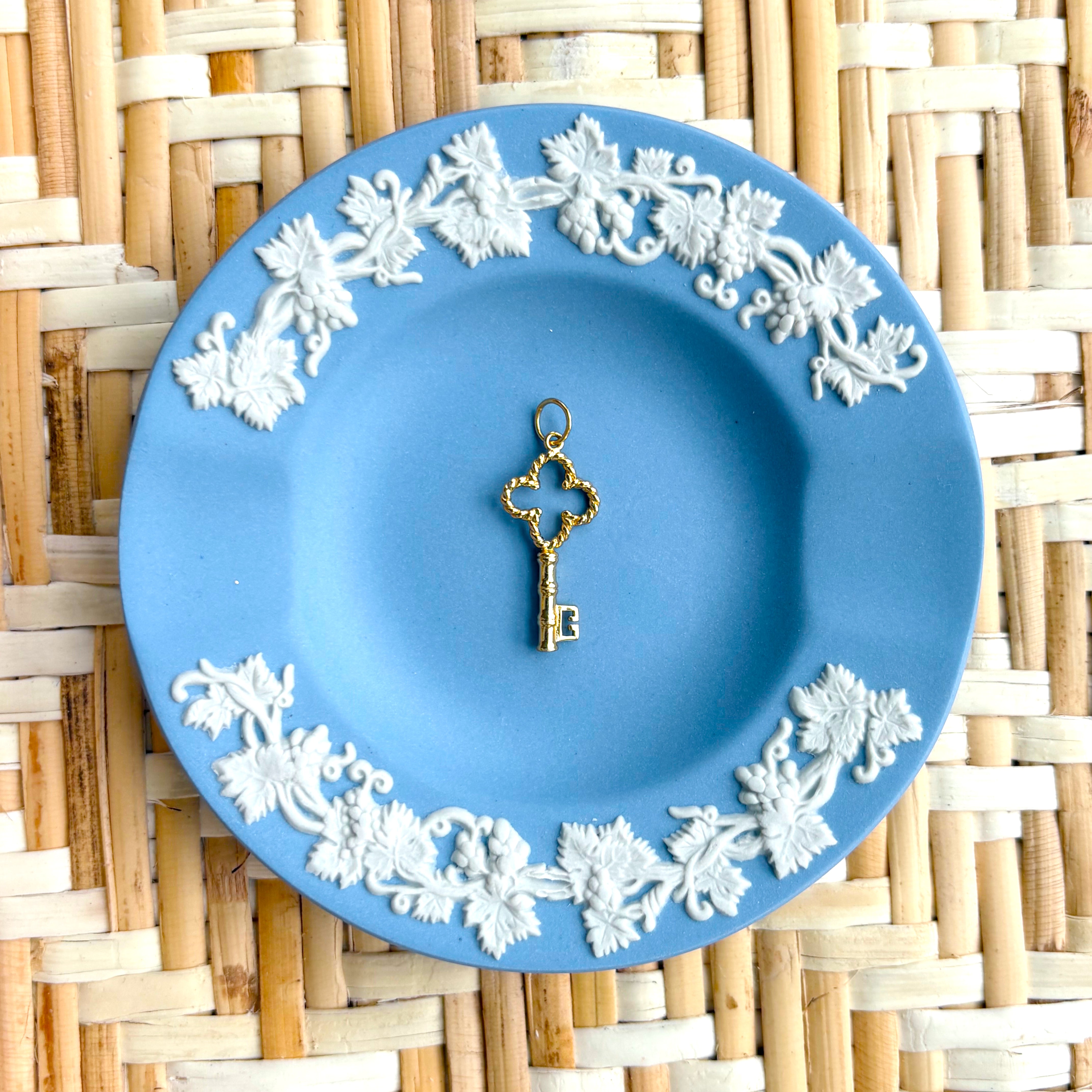 Decorative blue plate with white floral patterns and a golden key charm on a woven mat background