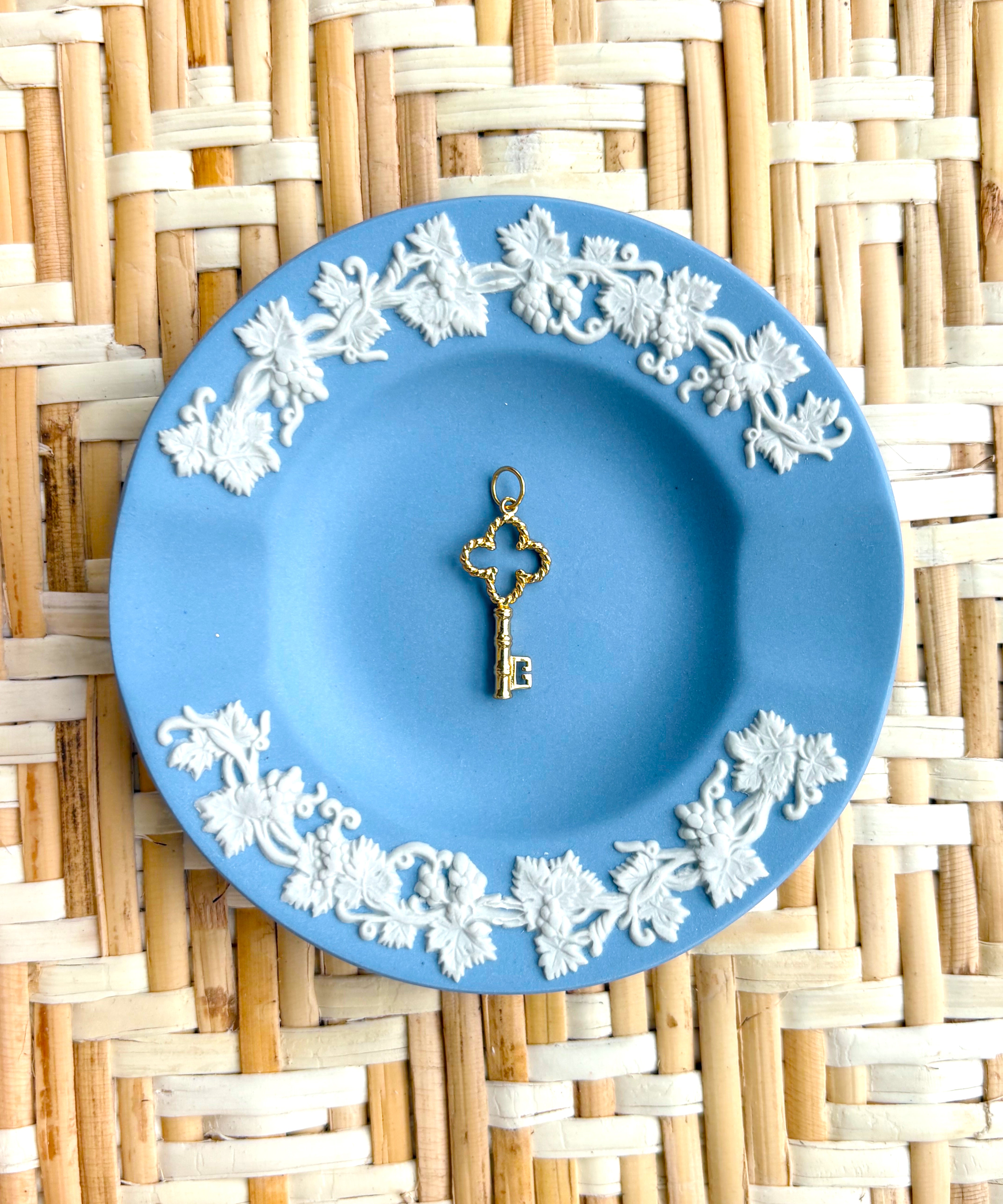 Decorative blue plate with white floral patterns and a golden key charm on a woven mat background