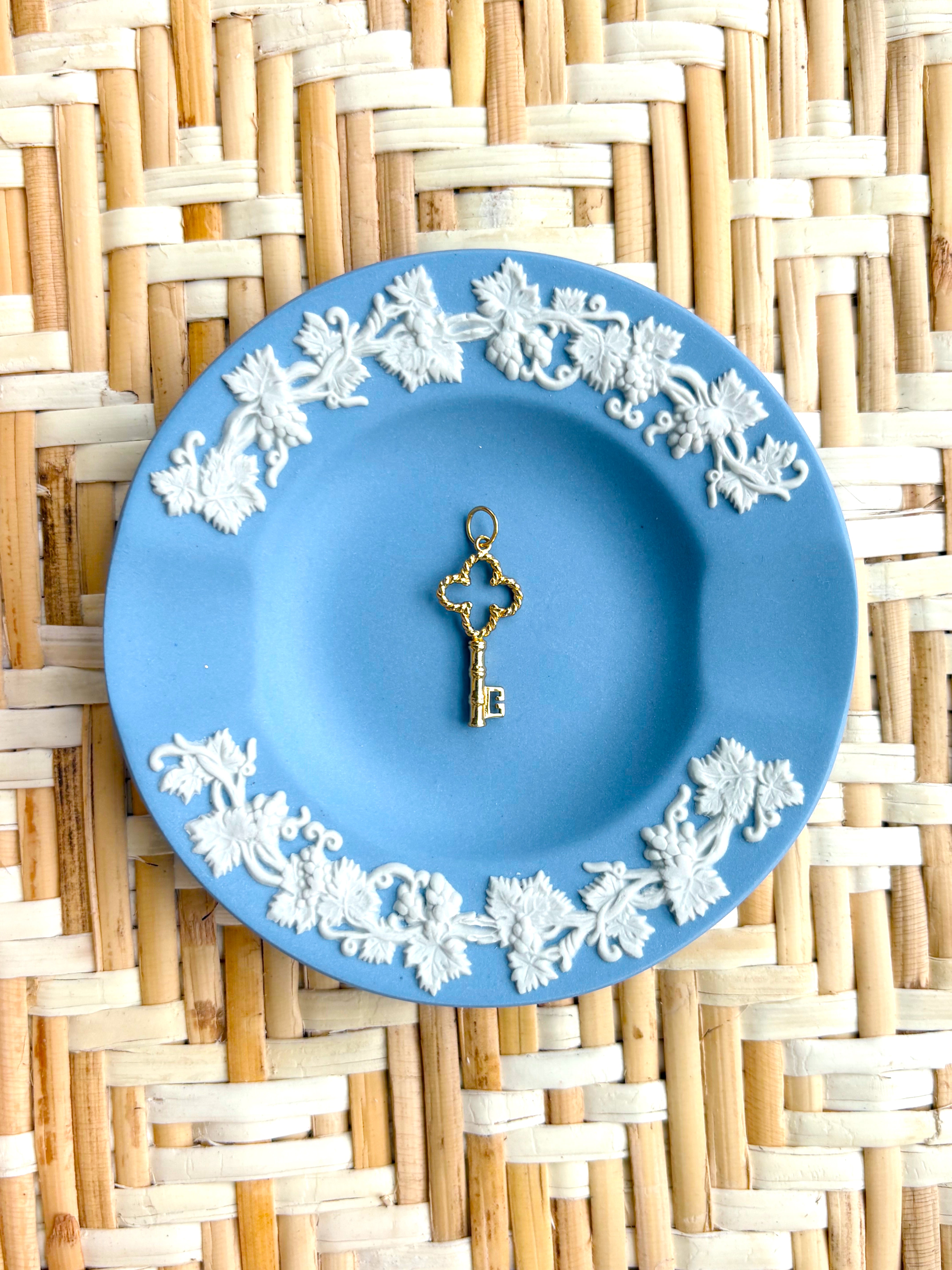 Decorative blue plate with white floral patterns and a golden key charm on a woven mat background