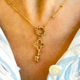 Golden necklace with a key pendant on a person wearing a light blue and white striped garment.