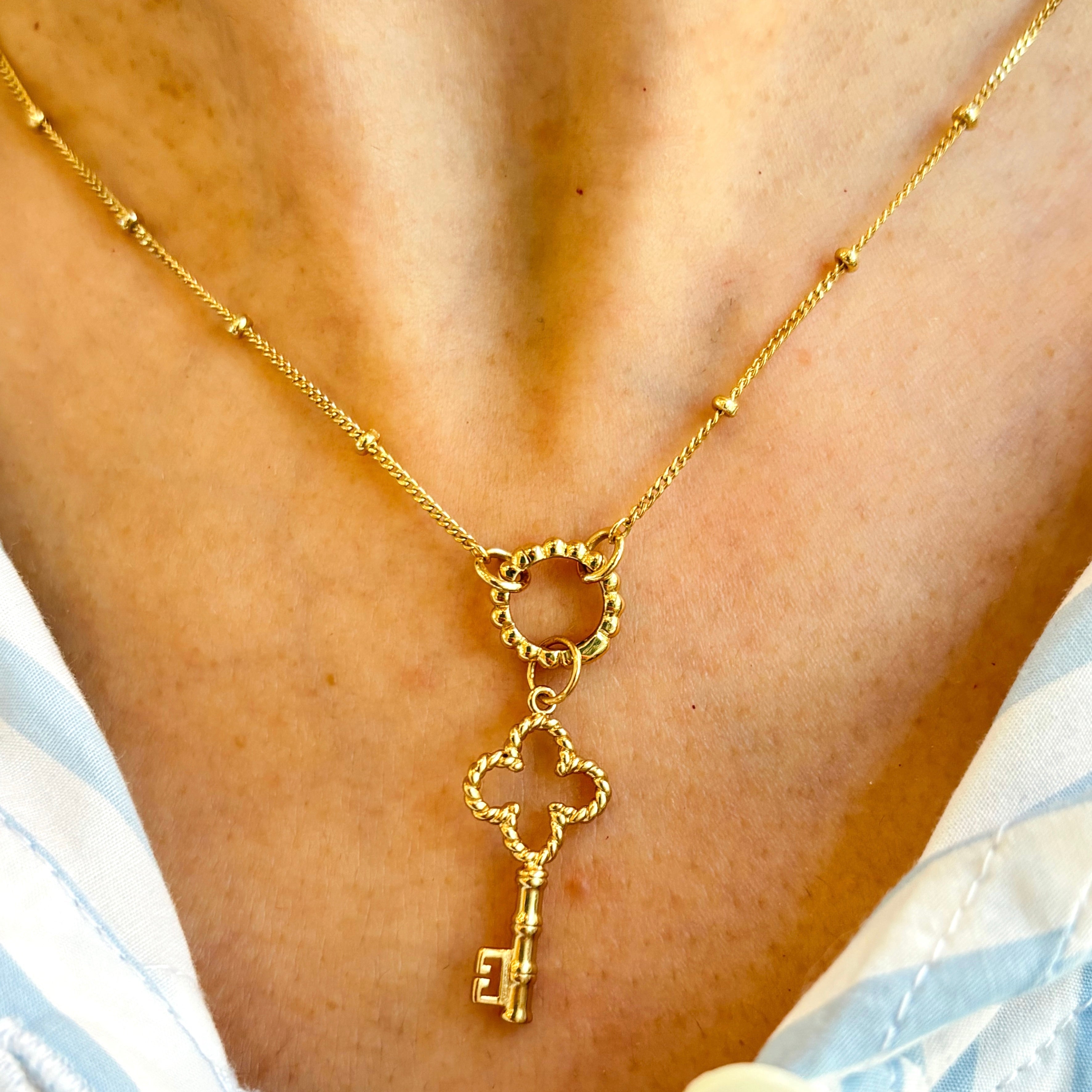 Golden necklace with a key pendant on a person wearing a light blue and white striped garment.