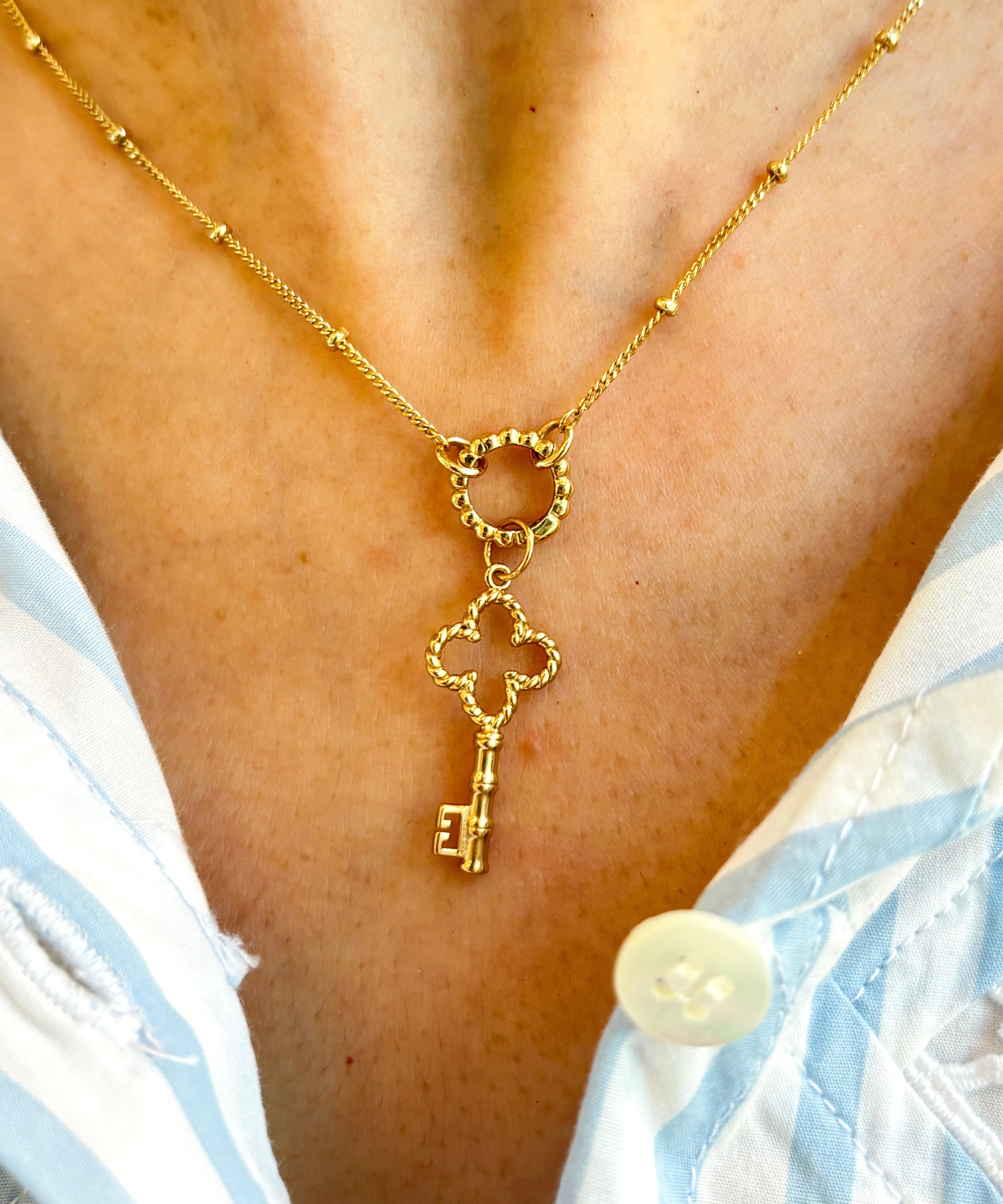 Golden necklace with a key pendant on a person wearing a light blue and white striped garment.