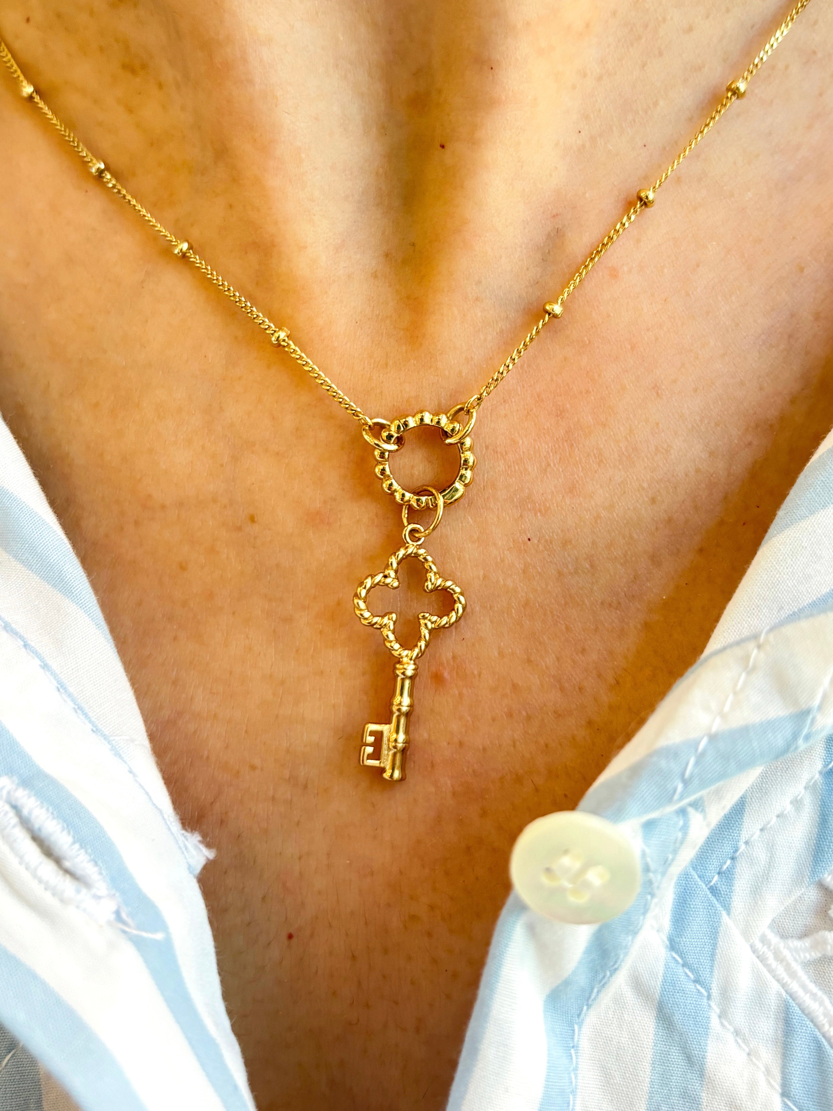 Golden necklace with a key pendant on a person wearing a light blue and white striped garment.