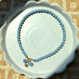 basket charm, blue flower charm, and a blue shell charm on a blue beaded necklace on a white plate
