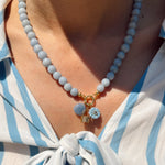 Necklace with blue and gold charms worn by a person in a white and blue striped shirt.