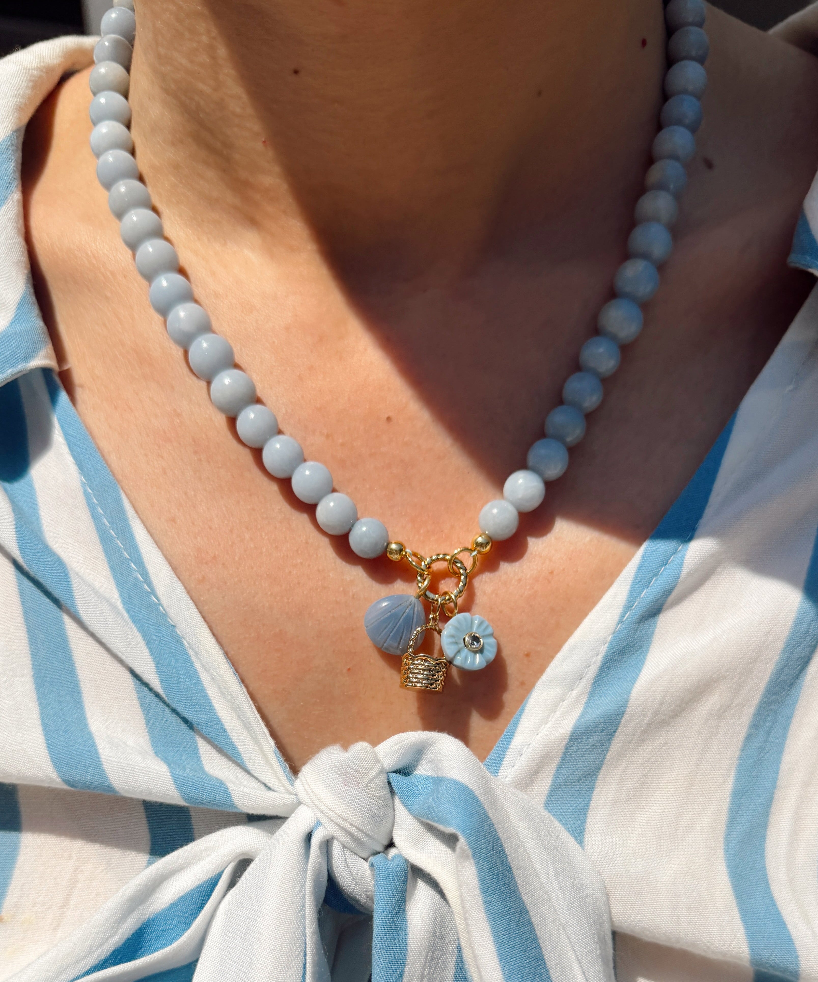 Necklace with blue and gold charms worn by a person in a white and blue striped shirt.