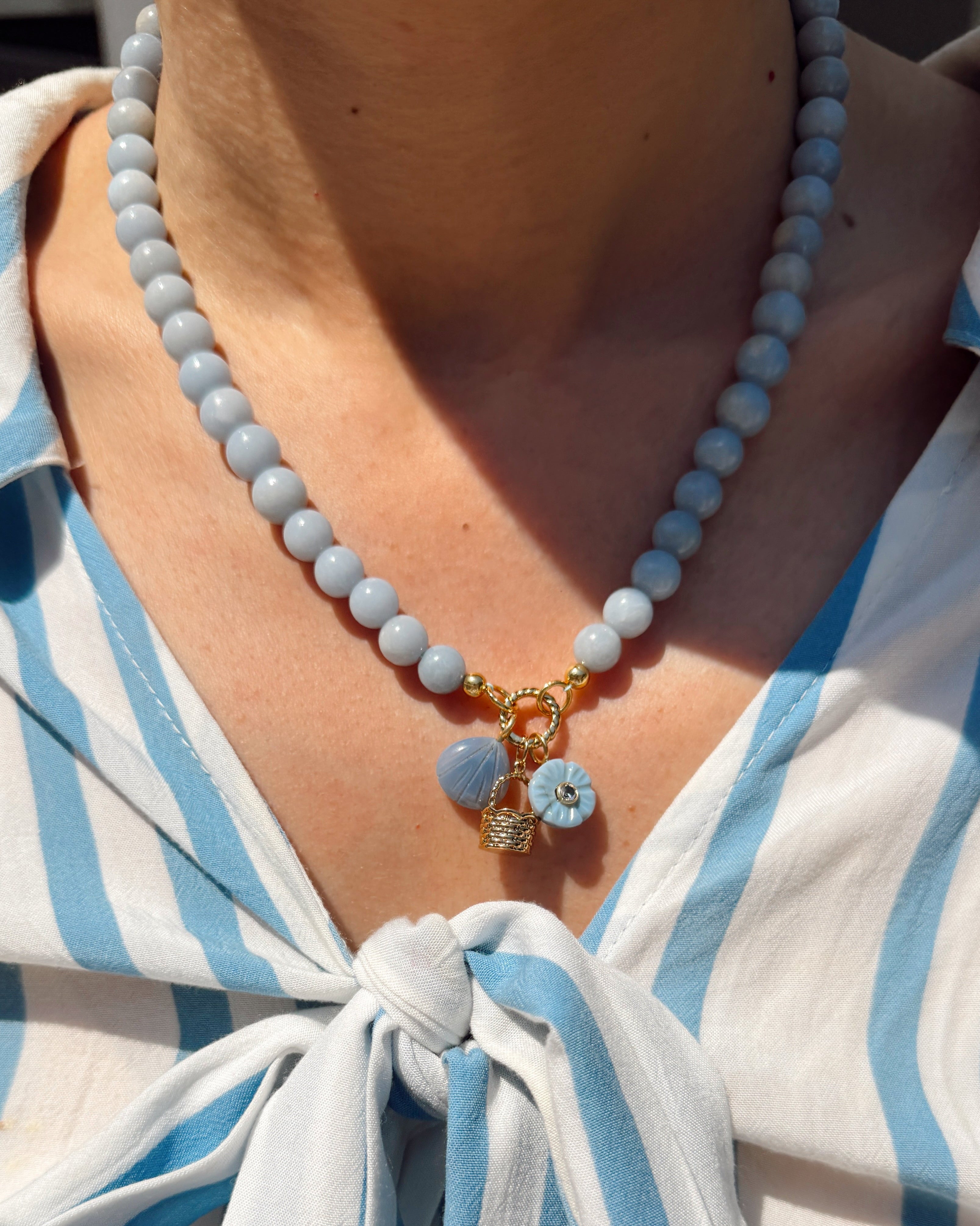 Necklace with blue and gold charms worn by a person in a white and blue striped shirt.
