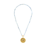 gold scalloped charm with blue gemstones on an aquamarine stone strand of beads