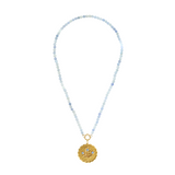 gold scalloped charm with blue gemstones on an aquamarine stone strand of beads