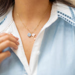 A close-up of a person wearing a delicate gold necklace with a light blue flower charm and key charm