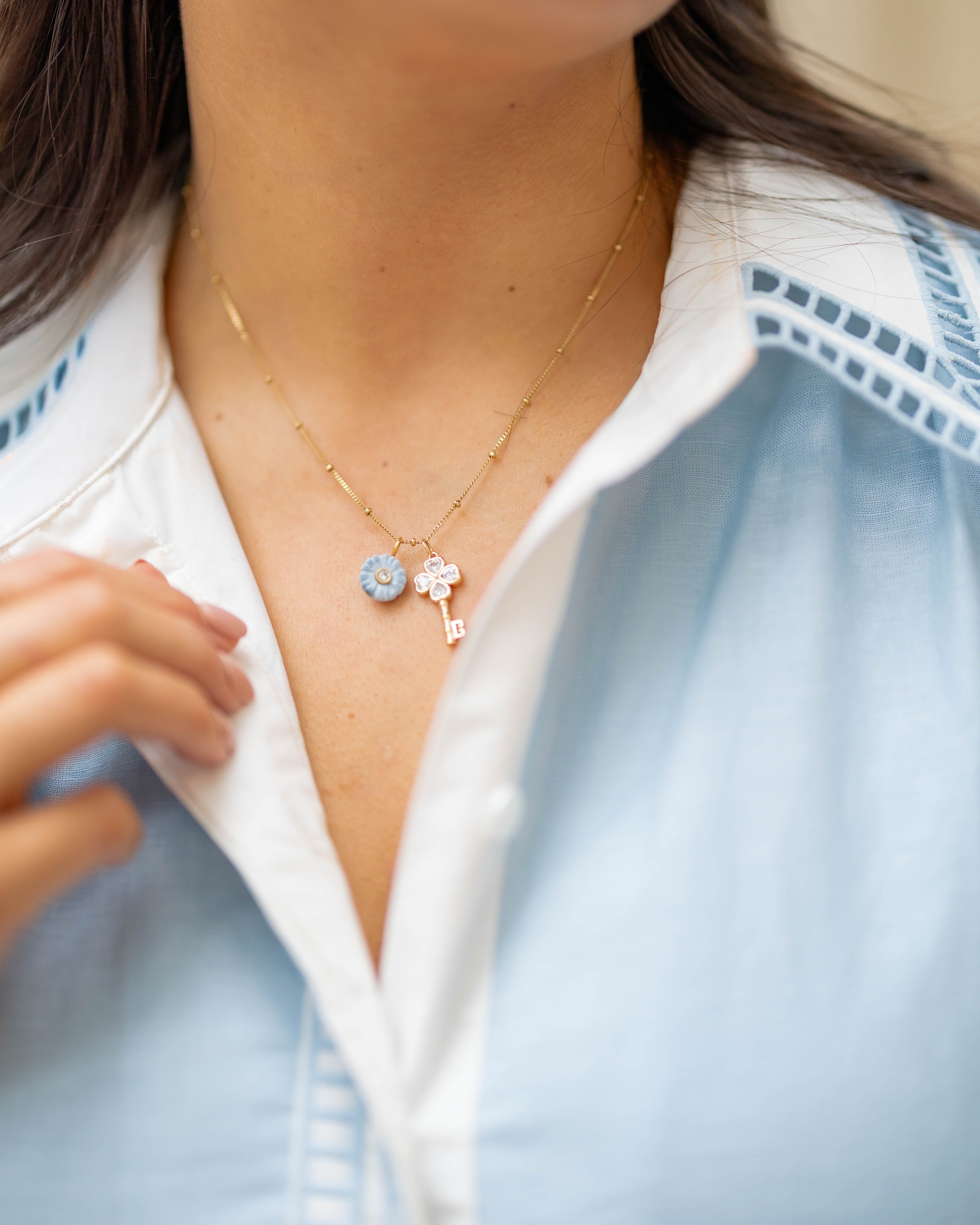 A close-up of a person wearing a delicate gold necklace with a light blue flower charm and key charm