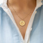 Gold necklace with a pendant worn by a person in a light blue shirt.