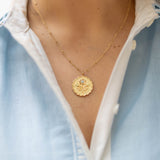 Gold necklace with a pendant worn by a person in a light blue shirt.