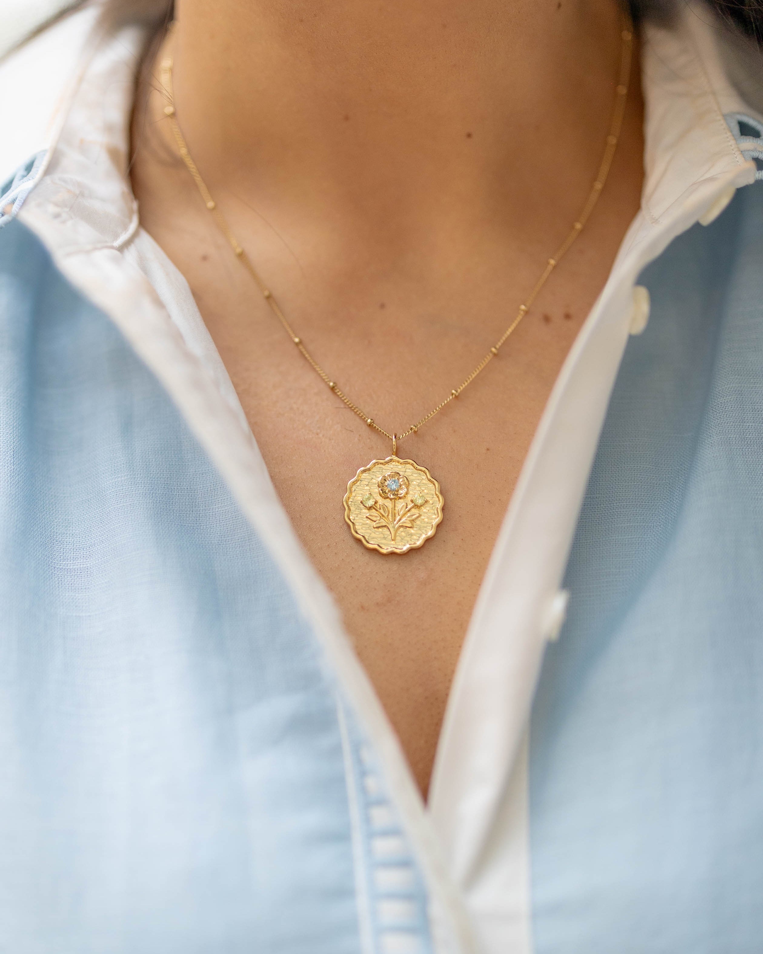 Gold necklace with a pendant worn by a person in a light blue shirt.