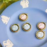 cameo pendant charms displayed on a blue plate with a flower in the background
