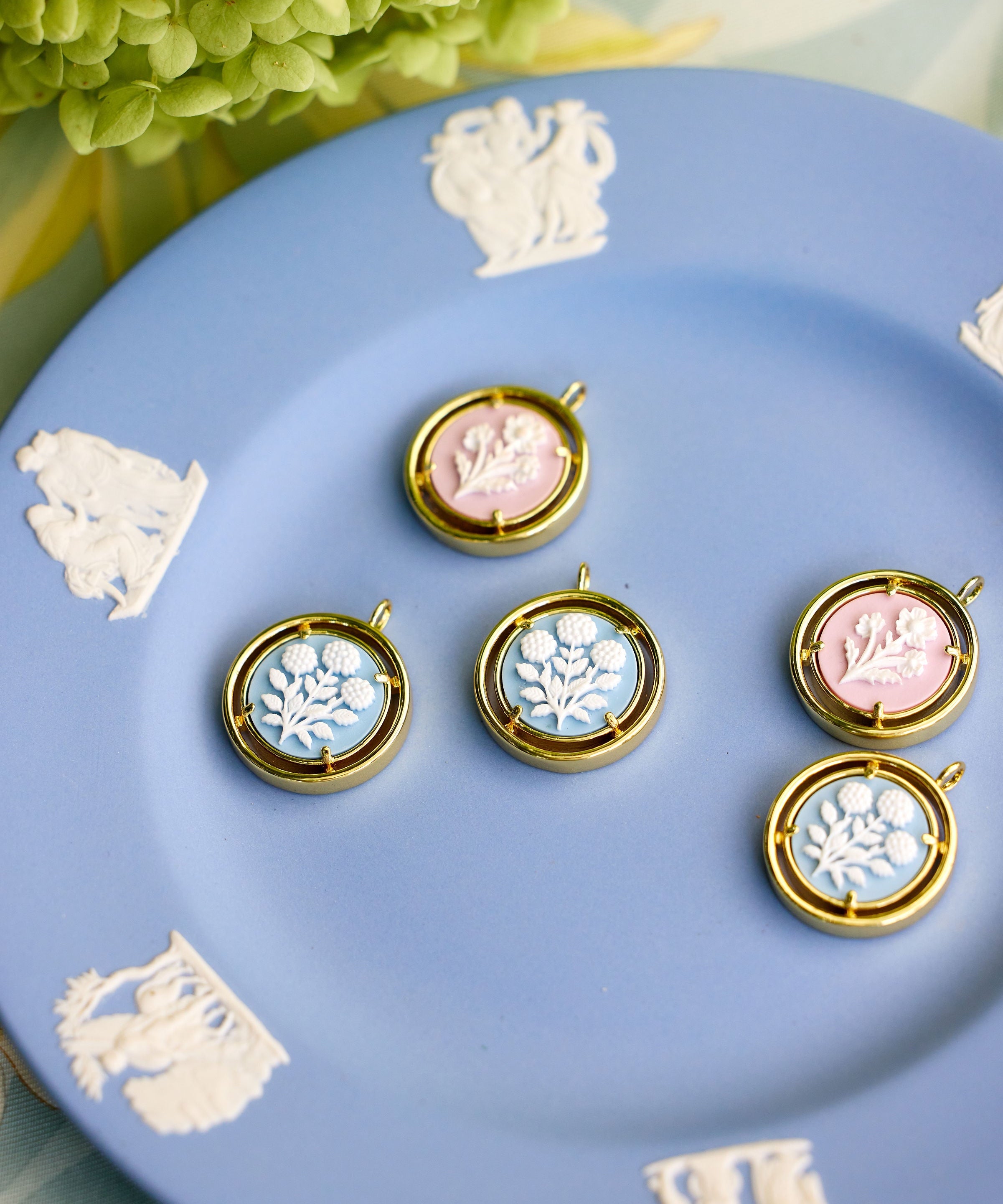 cameo pendant charms displayed on a blue plate with a flower in the background