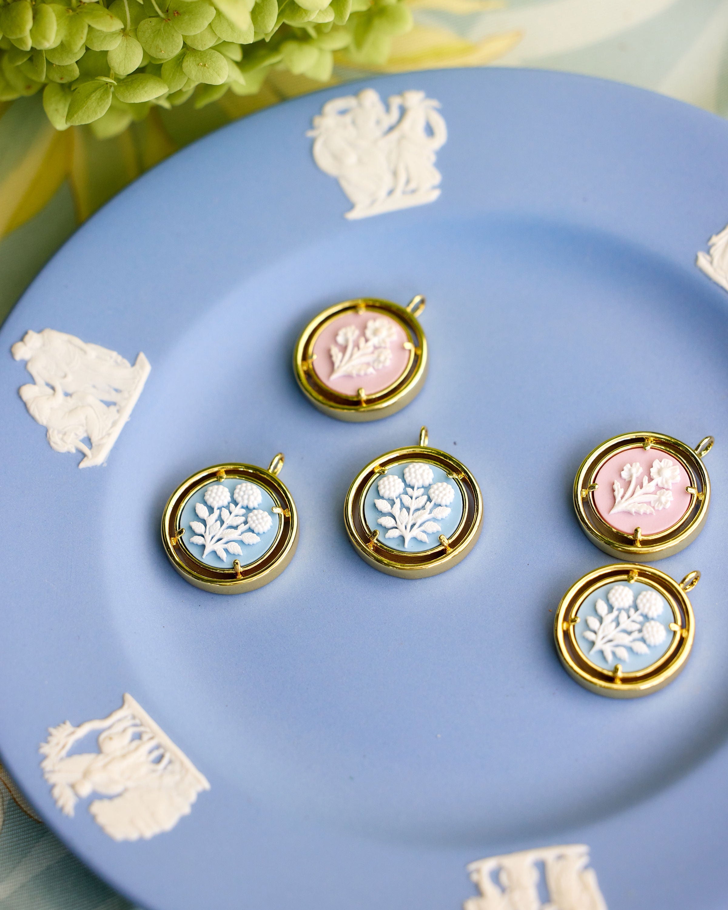cameo pendant charms displayed on a blue plate with a flower in the background