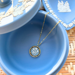 Blue jewelry dish with a gold necklace featuring a circular cameo pendant on a woven surface
