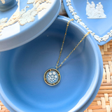 Blue jewelry dish with a gold necklace featuring a circular cameo pendant on a woven surface