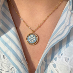 Necklace with a blue floral cameo pendant worn by a person in a striped shirt
