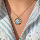 Necklace with a blue floral cameo pendant worn by a person in a striped shirt