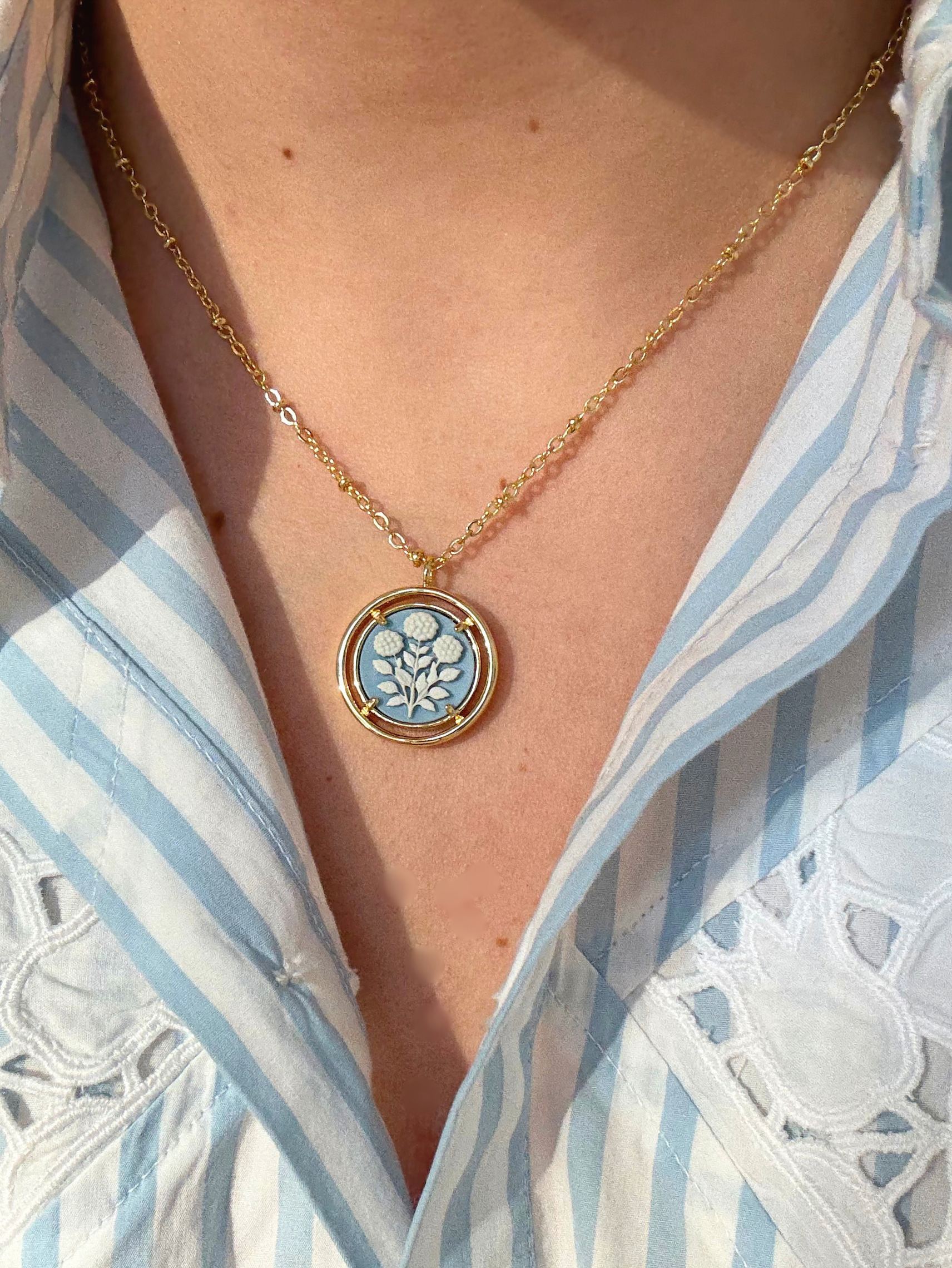 Necklace with a blue floral cameo pendant worn by a person in a striped shirt