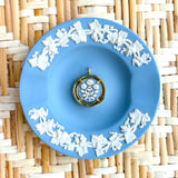 Blue decorative plate with white floral patterns on a woven mat background displaying a blue and white cameo pendant