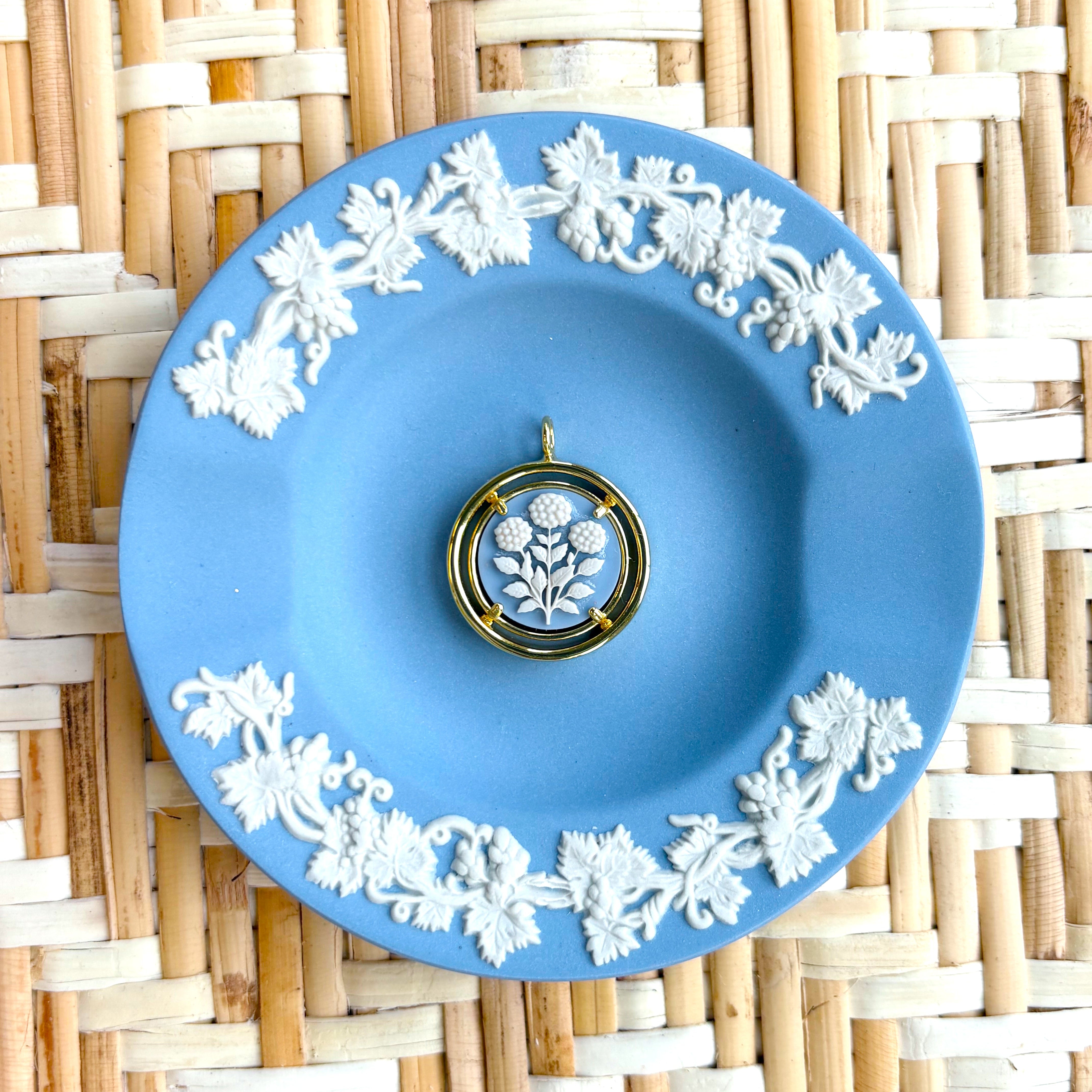 Blue decorative plate with white floral patterns on a woven mat background displaying a blue and white cameo pendant