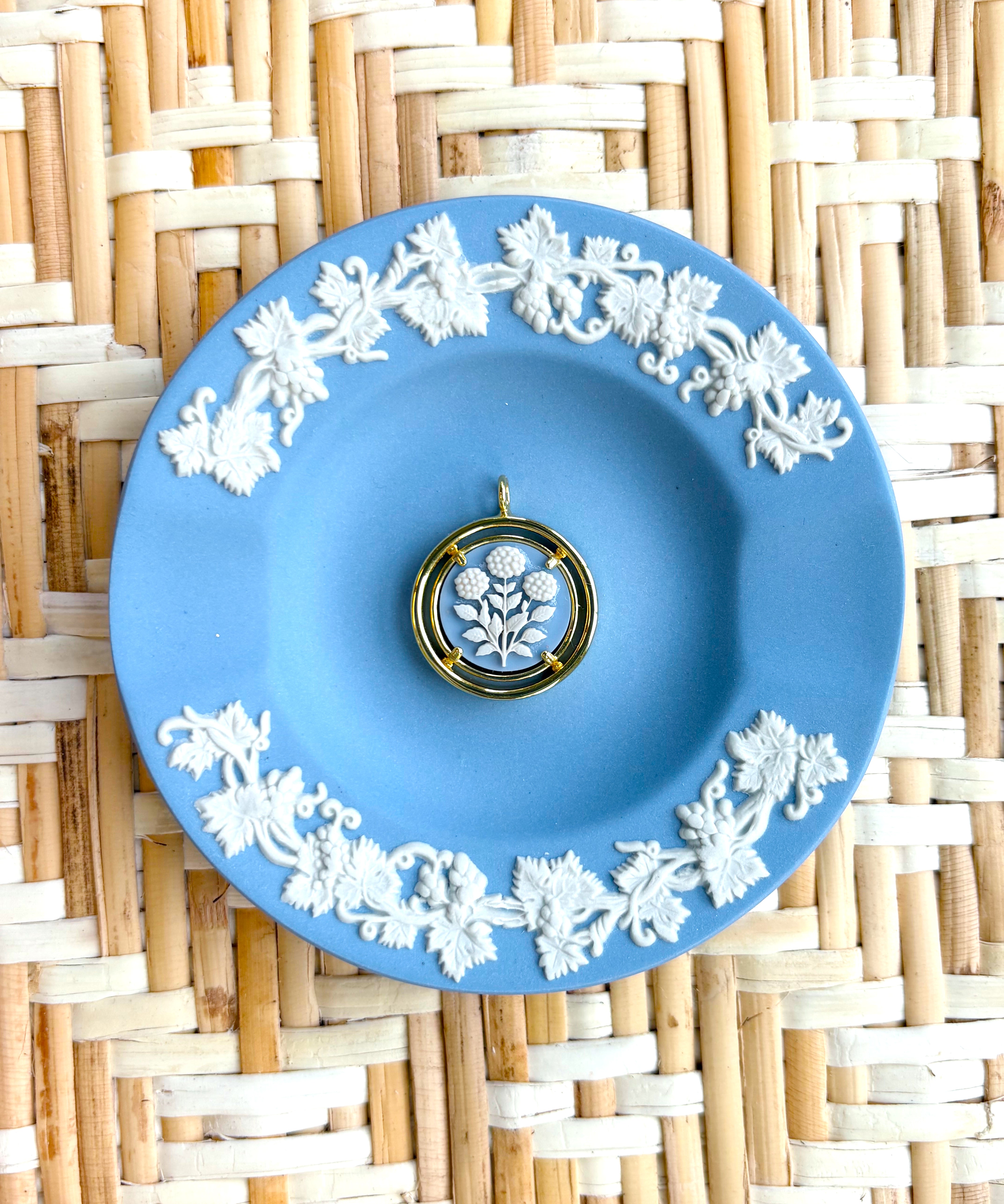 Blue decorative plate with white floral patterns on a woven mat background displaying a blue and white cameo pendant
