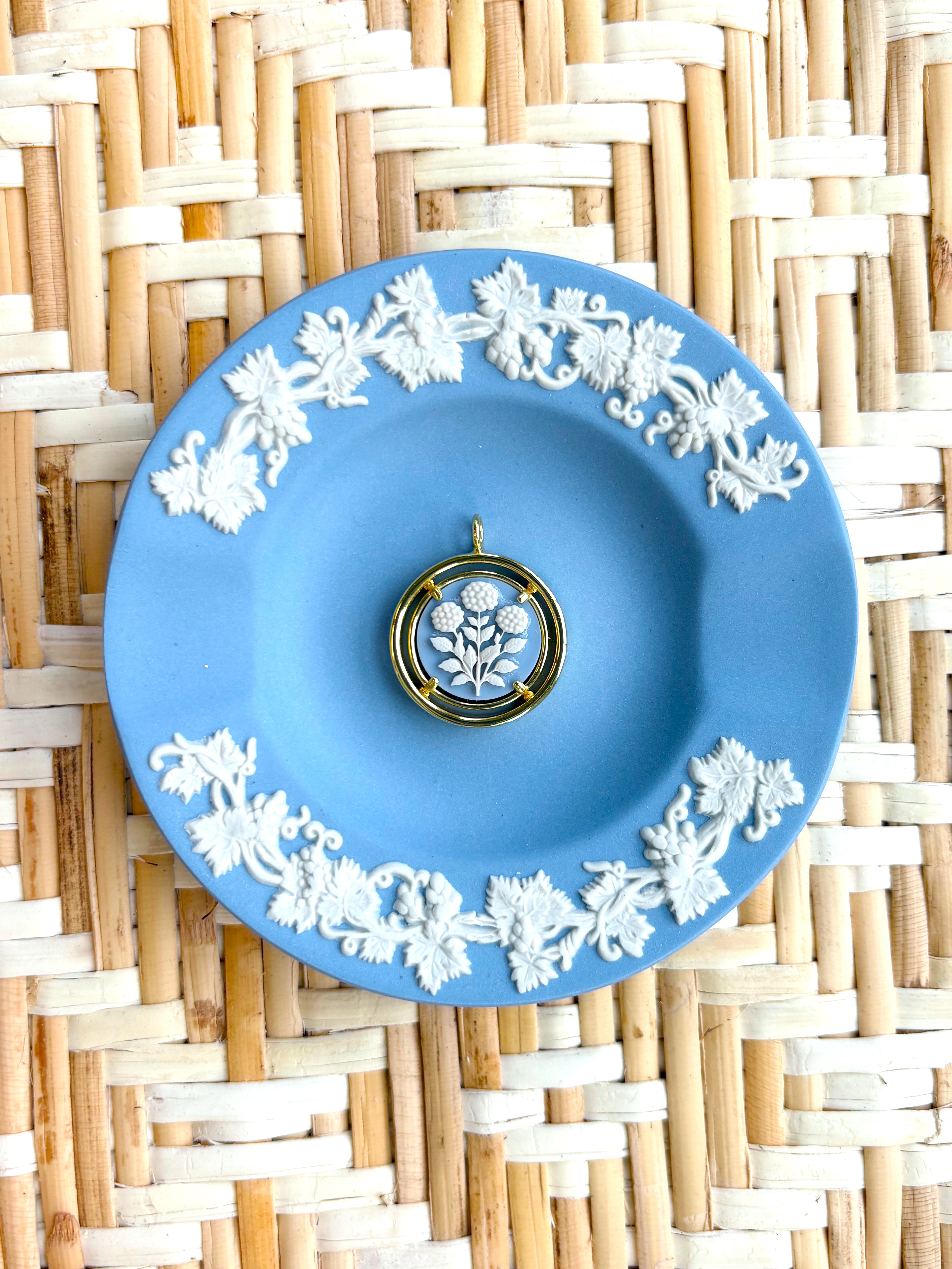 Blue decorative plate with white floral patterns on a woven mat background displaying a blue and white cameo pendant