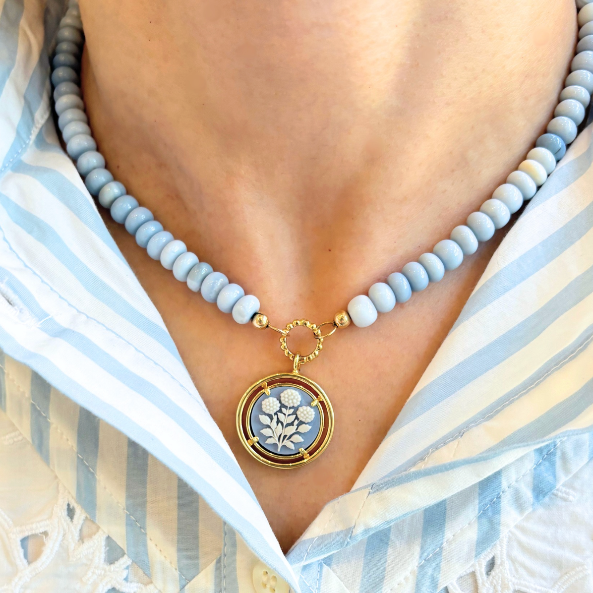 Necklace with a floral pendant worn by a person in a striped shirt