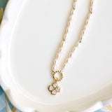 A delicate necklace with small white pearls and a gold four-leaf clover pendant set with clear crystals, resting on a white scalloped dish.