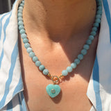 Necklace with a heart-shaped turquoise pendant worn by a person in a striped shirt.