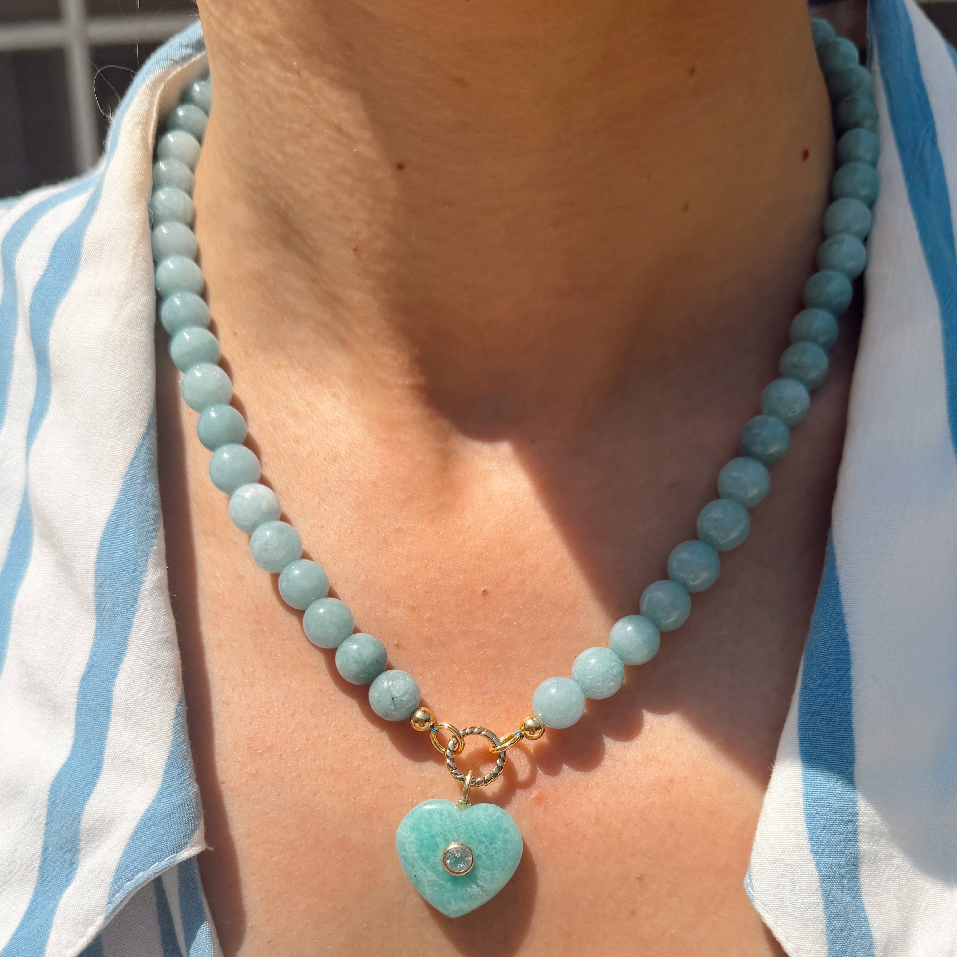 Necklace with a heart-shaped turquoise pendant worn by a person in a striped shirt.