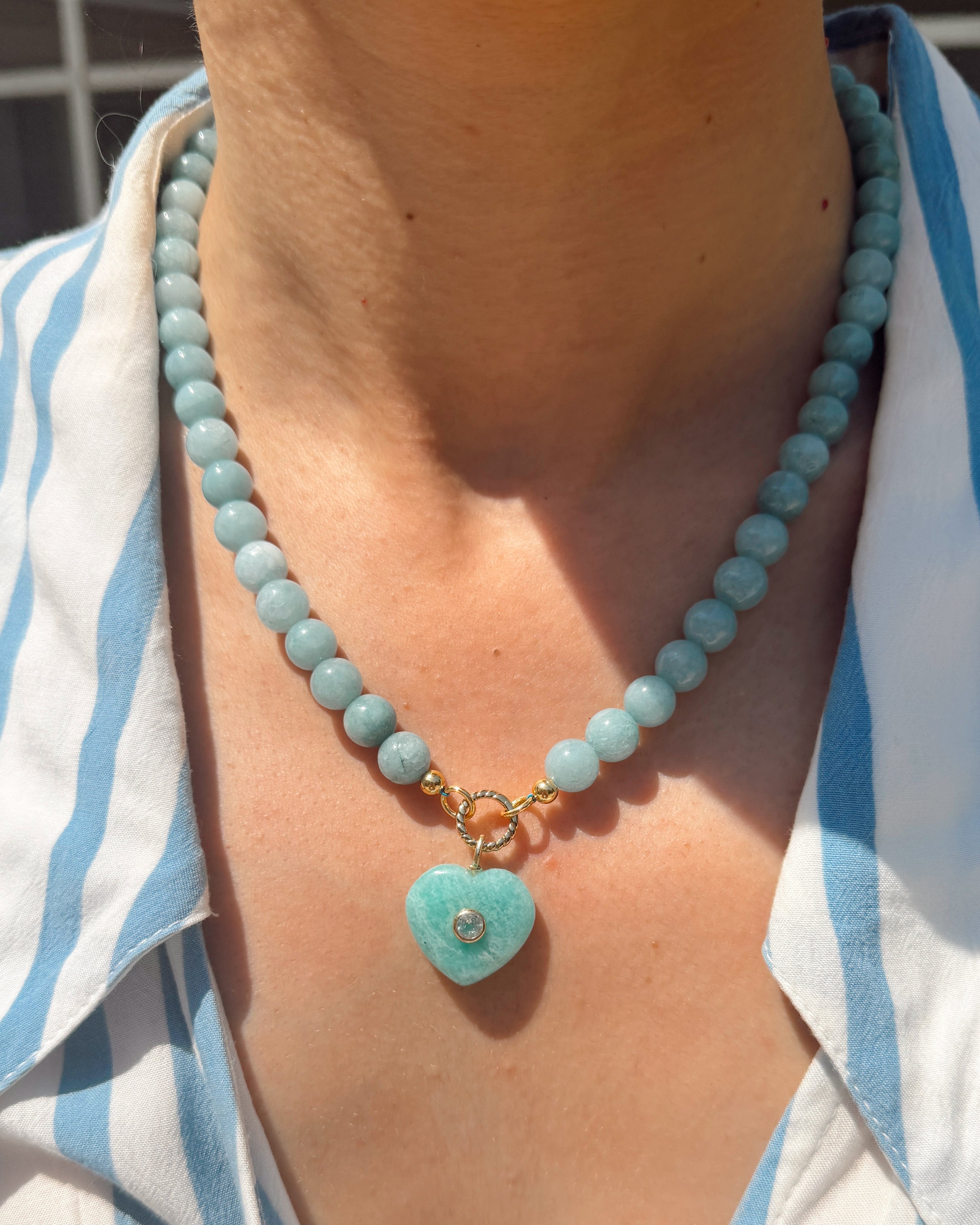 Necklace with a heart-shaped turquoise pendant worn by a person in a striped shirt.