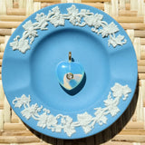 Blue decorative plate with white floral patterns on a woven surface displaying a heart charm