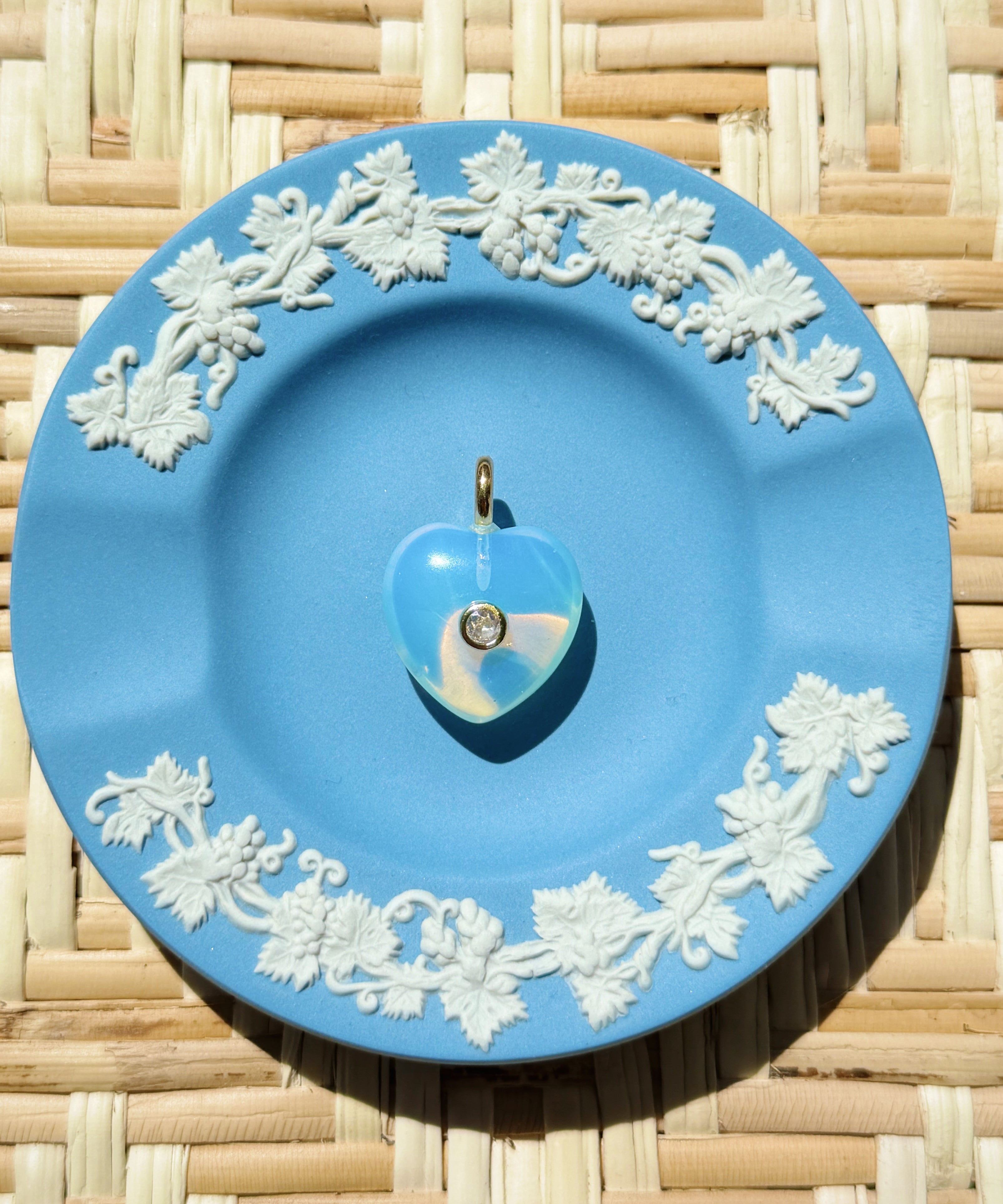 Blue decorative plate with white floral patterns on a woven surface displaying a heart charm