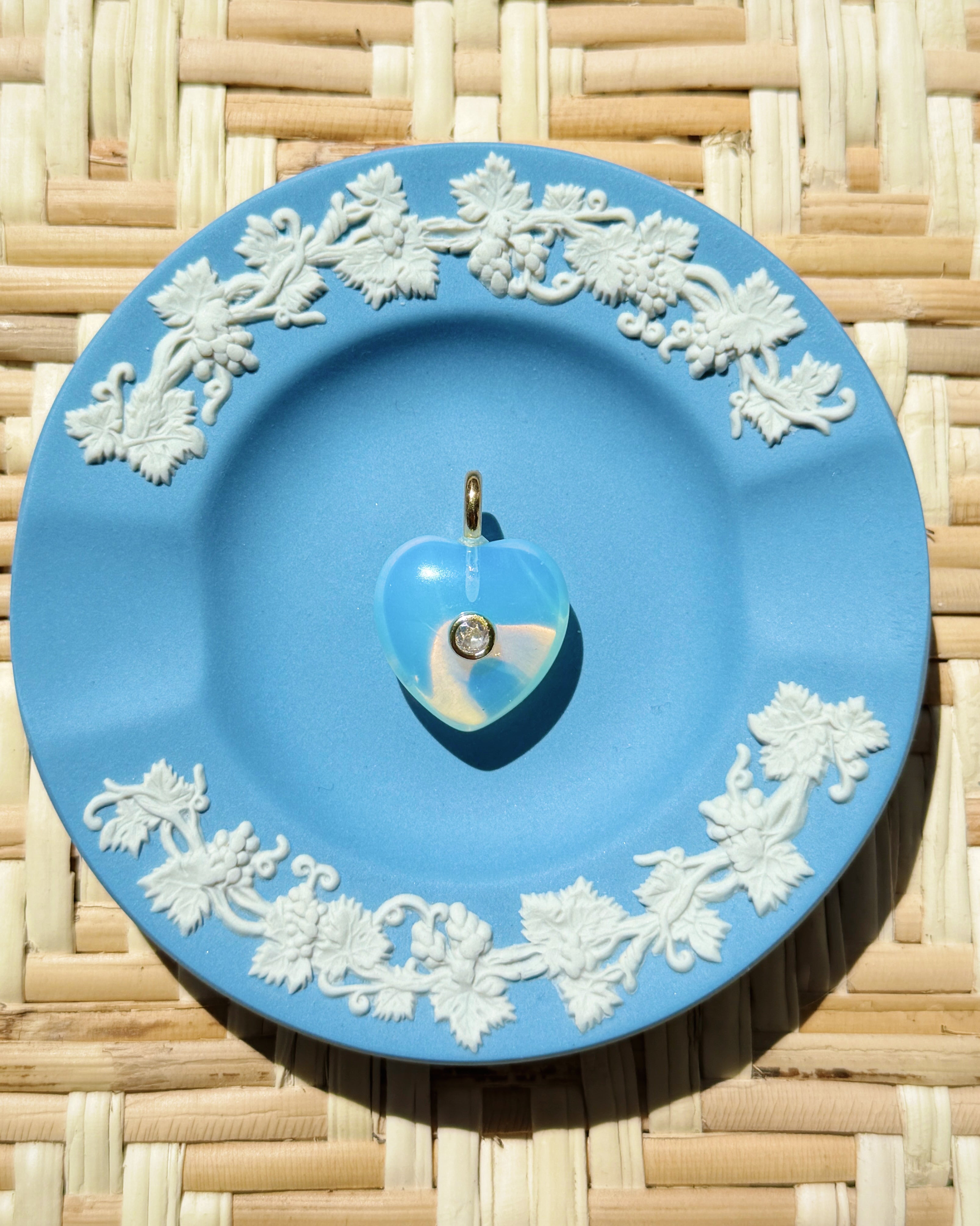 Blue decorative plate with white floral patterns on a woven surface displaying a heart charm